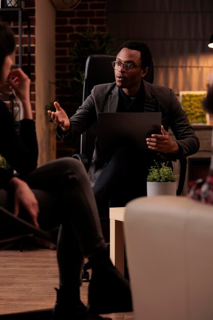 Young psychotherapist explaining psychological issues to people at couple therapy, using laptop to take psychoanalysis notes. Listening to conflict and finding solution to save marriage.