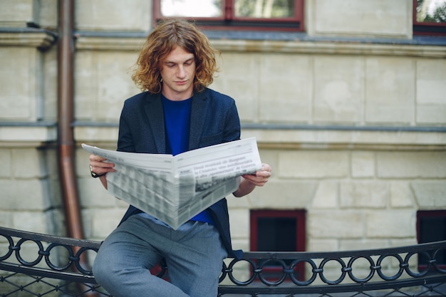 古いスタイルの建物の近くの新聞を読んで赤みを帯びた若者