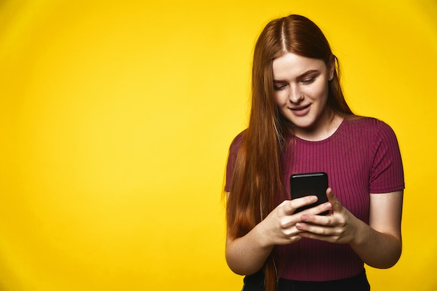 young redhead caucasian girl is happily looking on the cellphone