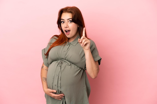 Молодая рыжая кавказская женщина изолирована на розовом фоне беременной и думающей Premium Фотографии
