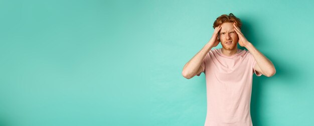 Free photo young redhead man touching head and looking dizzy feeling headache or migraine standing in tshirt ov