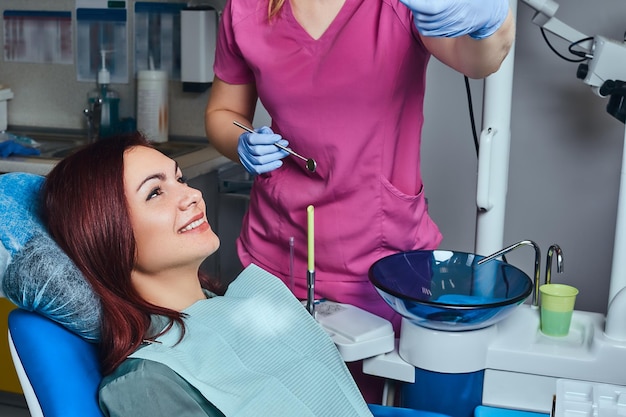 クリニックの歯科用椅子に座って診察を受けている若い赤毛の女性。