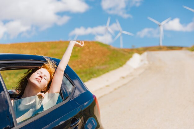 Young redhead woman loving life out of car window