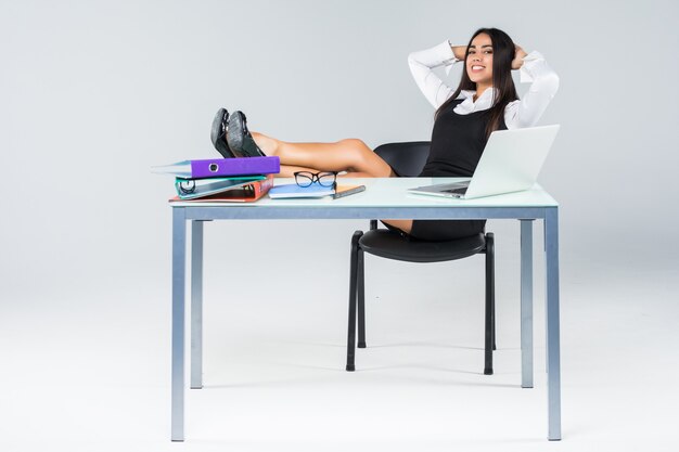 Young relaxed business woman with legs on working table enjoy the end of working day isolated on gray