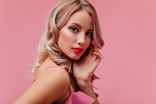 Молодая романтическая милая блондинка модельной внешности с ярким макияжем позирует для портрета на розовой изолированной стене