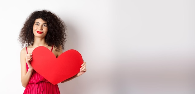 Free photo young romantic woman dreaming about love on valentines day looking for soulmate holding big red hear