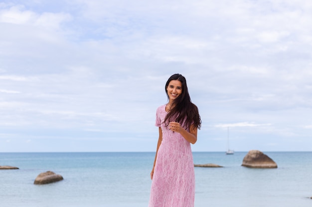 Foto gratuita giovane donna romantica con lunghi capelli scuri in un vestito sulla spiaggia sorridendo e ridendo divertendosi da solo