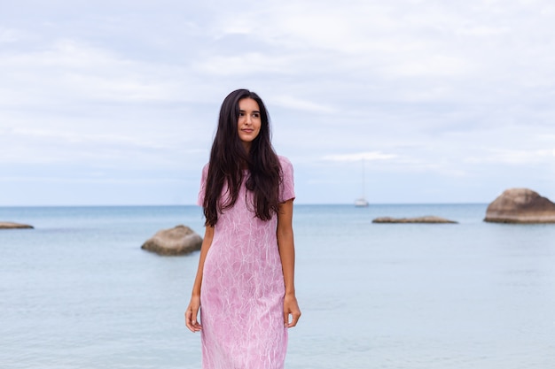 Young romantic woman with long dark hair in a dress on the beach smiling and laughing having a nice time alone