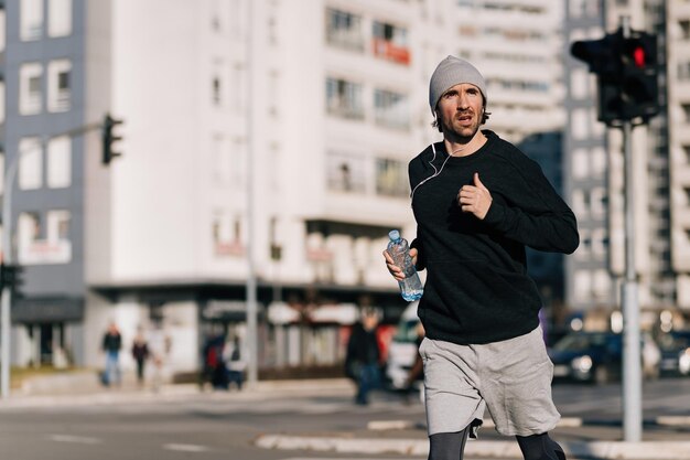 Young runner carrying bottle of water while jogging on the street