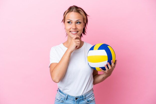 Молодая русская женщина играет в волейбол на розовом фоне и смотрит вверх