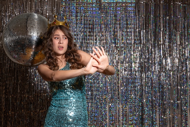 Foto gratuita giovane bella signora spaventata che indossa un abito blu verde lucido con paillettes con corona alla festa