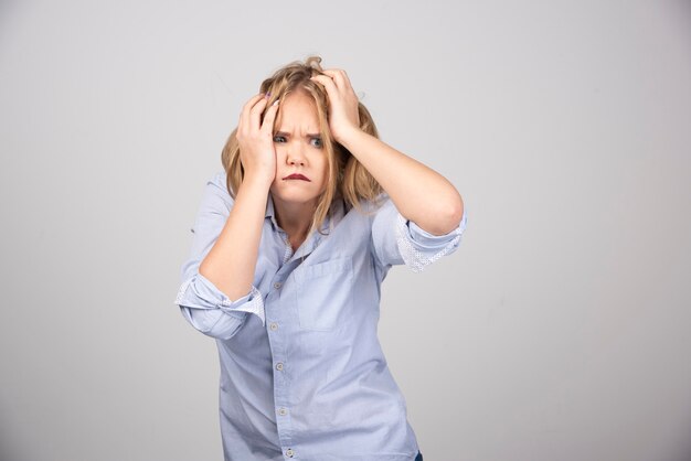 Young scared blonde woman with opened mouth holding hands on head.