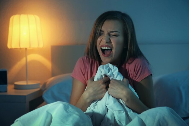 Молодая испуганная женщина, сидящая на кровати у себя дома