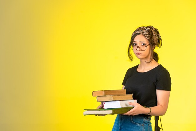 Foto gratuita giovane studentessa in occhiali che tiene i suoi libri e sembra stanca e annoiata.