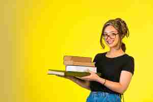 Foto gratuita giovane studentessa in occhiali tenendo i suoi libri e sorridendo positivamente.