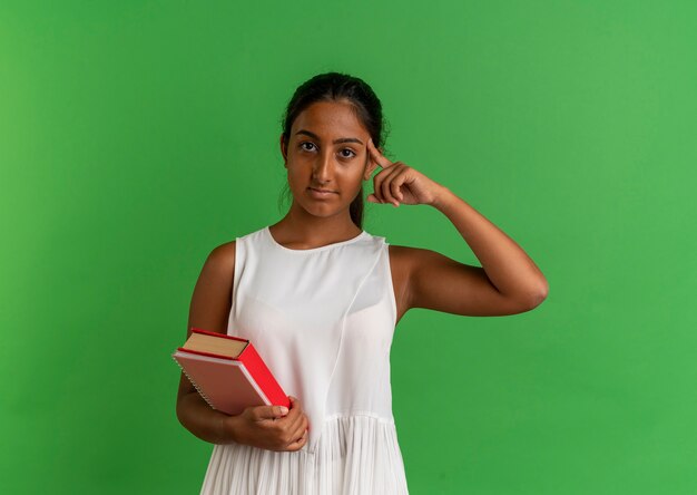 young schoolgirl holding book with notebook and putting finger on head 