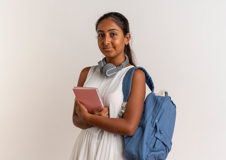 Free Photo young schoolgirl wearing back bag and headphones holding notebook on white