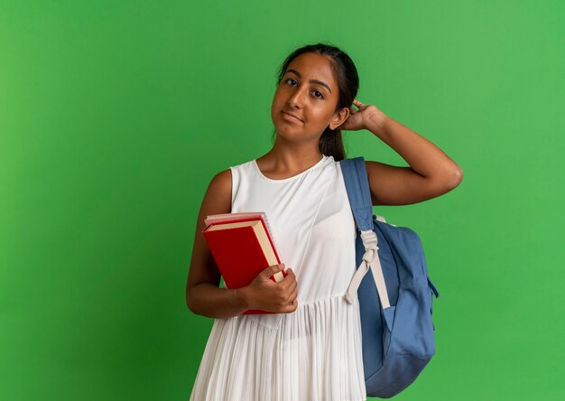 Free photo young schoolgirl wearing backpack holding book with notebook and putting hand on head