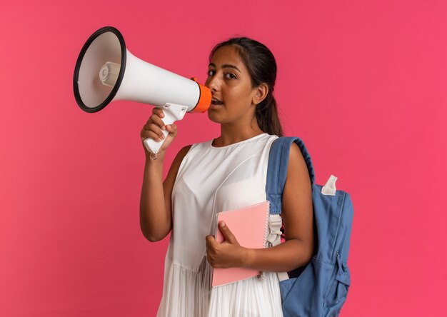 young schoolgirl wearing backpack holding notebook and speaks on loudspeaker 