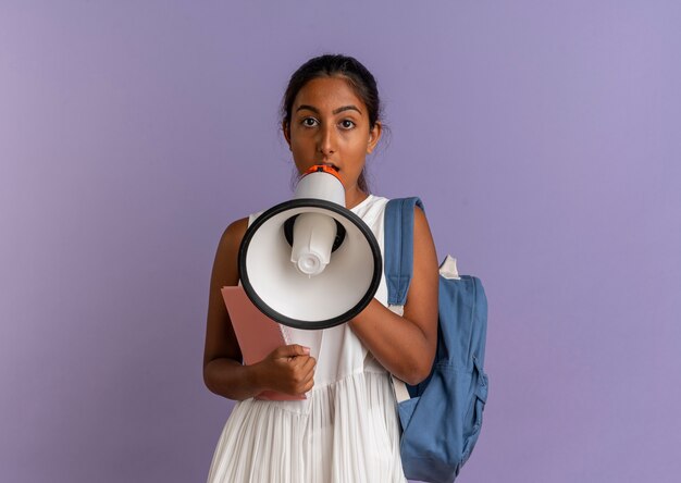 young schoolgirl wearing backpack holding notebook and speaks on loudspeaker