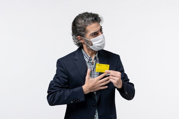 Young self-determined serious office assistant in suit wearing mask and holding his bank card on isolated white background