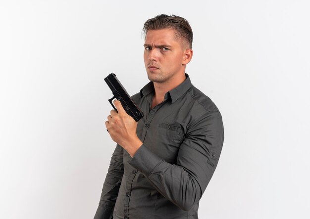 Young serious blonde handsome man holds gun isolated on white background with copy space