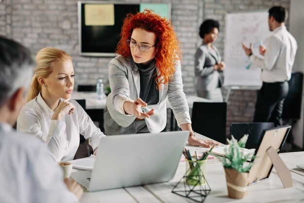 Young serious businesswoman pointing at something on laptop while having a meeting with her colleagues in the office