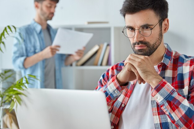 Young serious handsome man entrepreneur focused into portable laptop computer, prepares business project for meeting