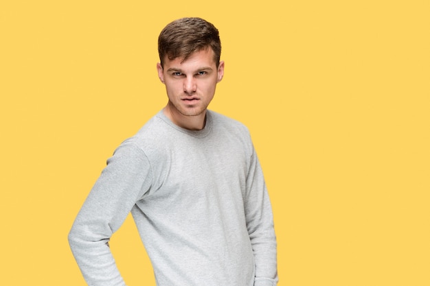 Free photo the young serious man looking cautiously on yellow studio