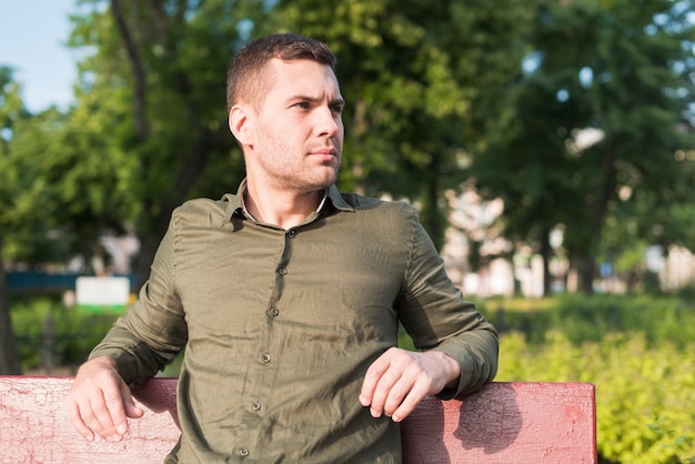 Young serious man sitting on bench in park