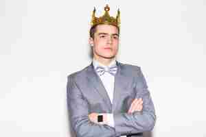 Free photo young serious man in suit and tie, holding golden crown over his head, on white wall