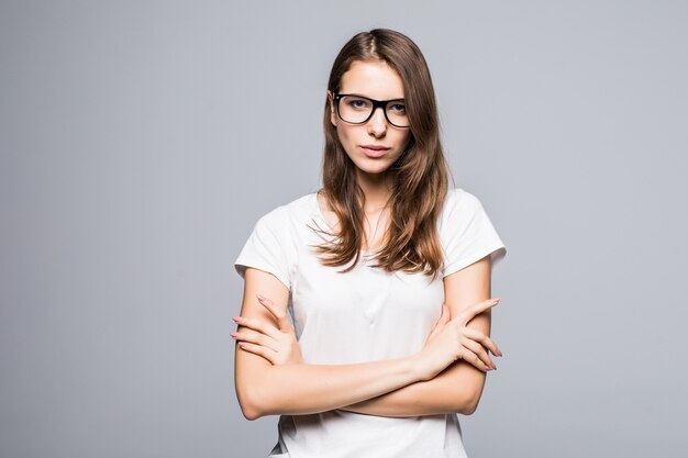Молодая серьезная думающая дама в очках в белой футболке и синих джинсах остается перед белым фоном студии