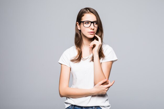 Young serious thinking lady in glasses in white t-shirt and blue jeans stay in front of white studio background