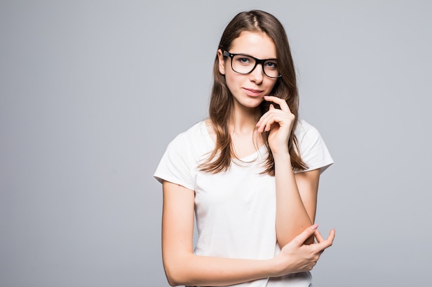 Young serious thinking lady in glasses in white t-shirt and blue jeans stay in front of white studio background