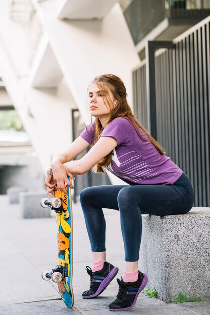 Young serious woman leans on skateboard