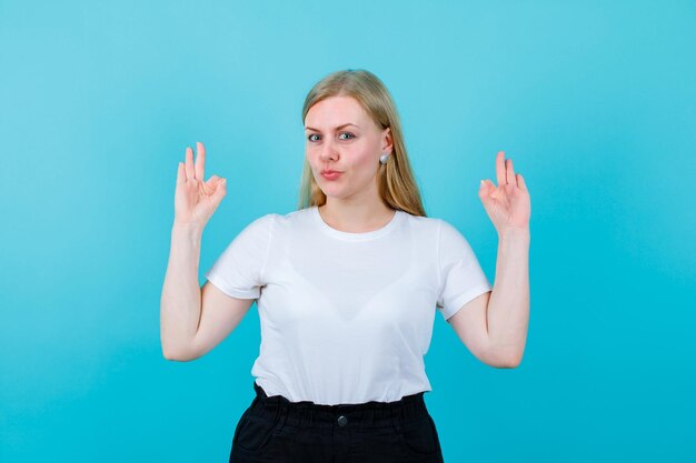 Young seriously girl is showing okay gestures on blue background
