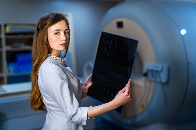 Молодой seriuos компетентная женщина-врач, глядя на рентгеновский снимок в кабинете врача. фон компьютерной томографии.