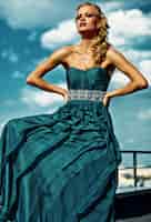 無料写真 青い空でポーズのイブニングドレスの若いセクシーな金髪の女性モデル