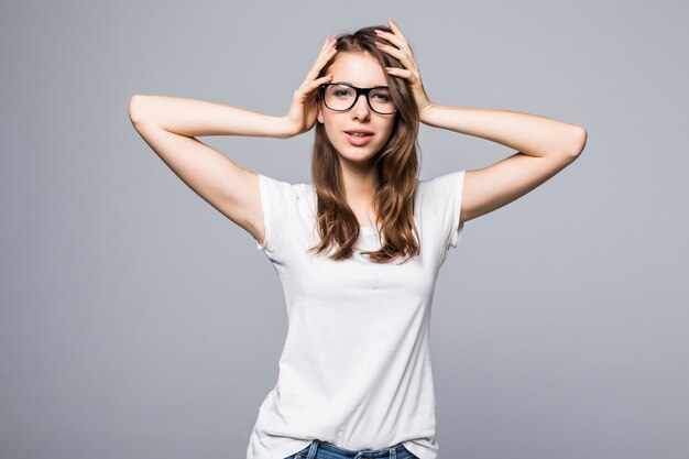 Young sexy lady in glasses in white t-shirt and blue jeans holds her arms on hair in front of white studio background