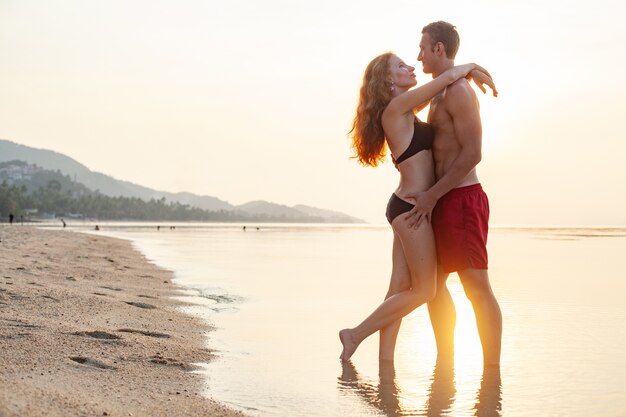 Молодая сексуальная романтическая влюбленная пара счастлива на летнем пляже, вместе веселясь в купальных костюмах