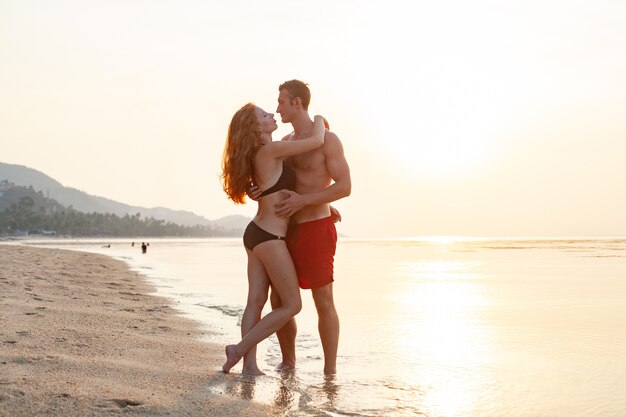 Young sexy romantic couple in love happy on summer beach together having fun wearing swim suits