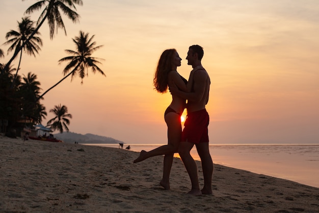 一緒に水着を着て楽しんで夏のビーチで幸せな夕日に恋をしている若いセクシーなロマンチックなカップル