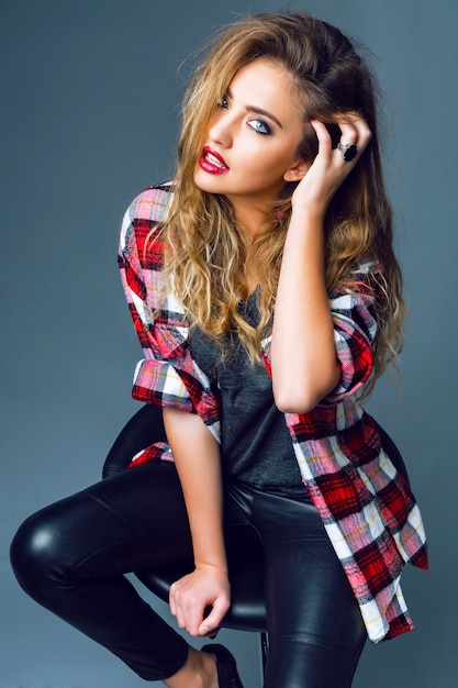 Young sexy woman model wearing stylish trendy leather pants and grunge hipster plaid shirt posing, have fluffy blonde hairs and smoky bright makeup. Rock n roll fashion style.