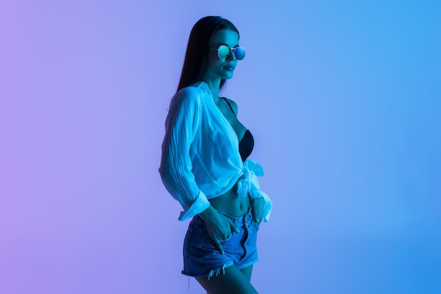 Free photo young sexy woman in short and shirt, sunglasses standing isolated on pink light