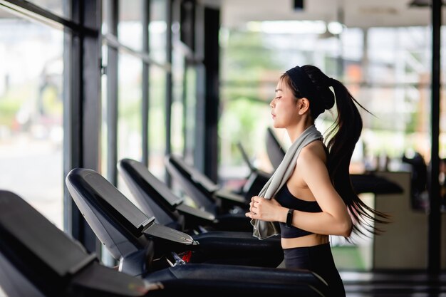 운동복, 땀 방지 직물 및 현대 체육관에서 운동하기 위해 러닝 머신에서 실행되는 스마트 워치를 착용하는 젊은 섹시한 여자, 미소, 복사 공간