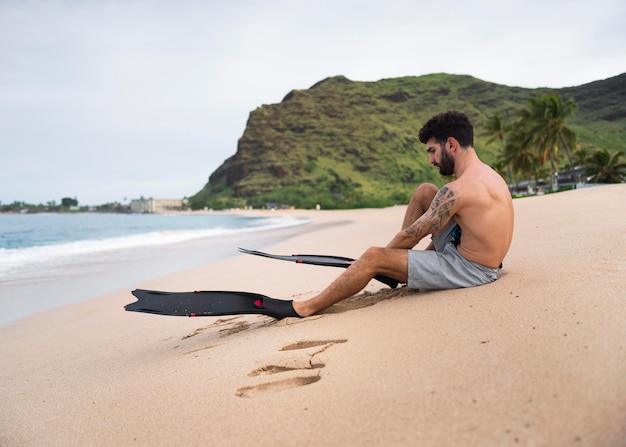 Foto gratuita giovane uomo a torso nudo sulla spiaggia con attrezzatura subacquea