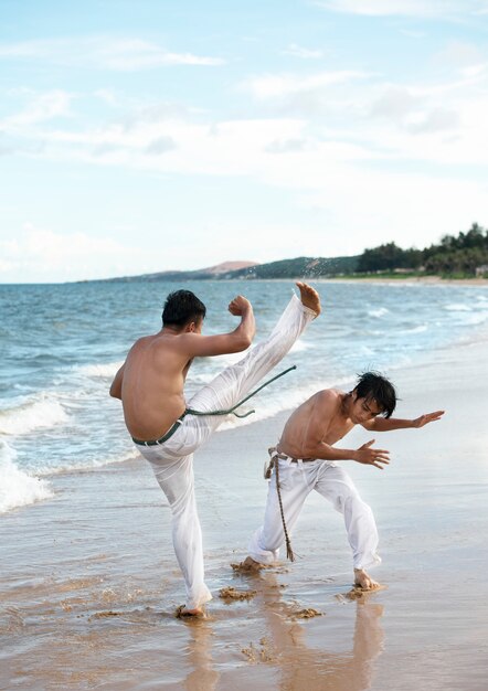 young shirtless men practicing capoeira together on the beach