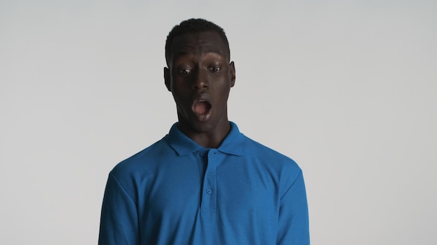 Молодой шокированный афроамериканец с открытым ртом выглядит пораженным перед камерой на белом фоне Вау, лицо