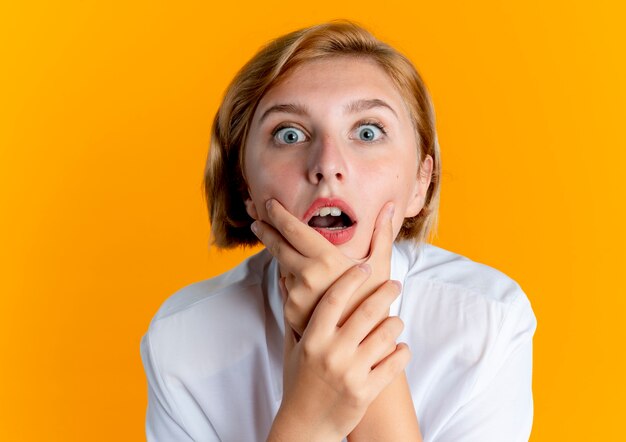 young shocked blonde russian girl holds chin looking at camera