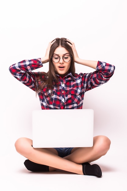 A young shocked woman sitting on the floor with a laptop on white